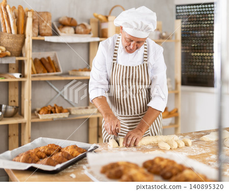 Baker in uniform cutting raw dough with knife to make croissants or buns Baker in uniform cutting raw dough with knife to make croissants or buns 140895320