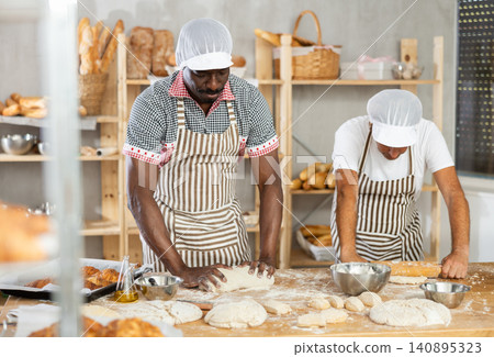 Two male bakers kneading dough and rolling it out 140895323
