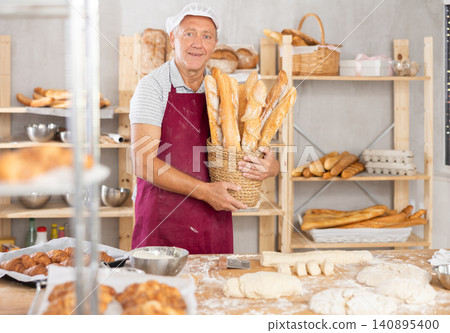 Bakery mature man employee holds basket of ready-made baguettes. 140895400