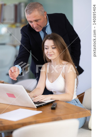 Mature male manager helping to woman during working at laptop in office Mature male manager helping to woman during working at laptop in office 140895404