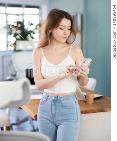 Young woman holding a mobile phone in her hands against the background of the office. Young woman holding a mobile phone in her hands against the background of the office. 140895454