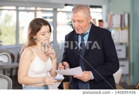 Elderly man and young women colleagues discussing document Elderly man and young women colleagues discussing document 140895456