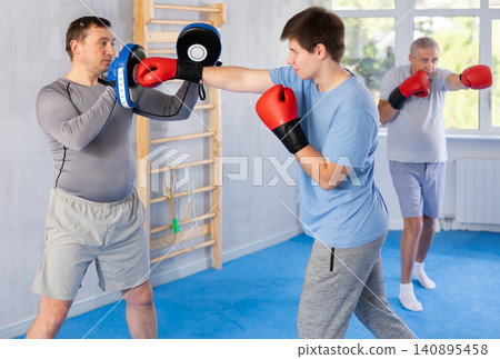 Boxing training - young guy masters boxing strikes on trainer punch mitts during training Boxing training - young guy masters boxing strikes on trainer punch mitts during training 140895458