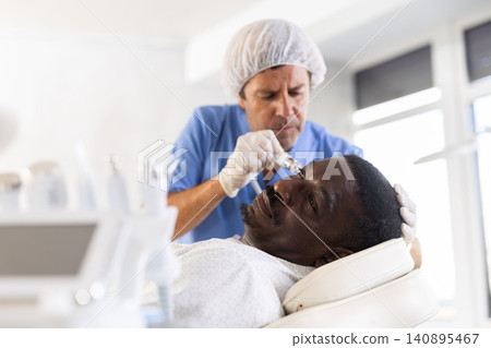 Male cosmetologist performs skin cleansing procedure for African man client with beauty machine 140895467