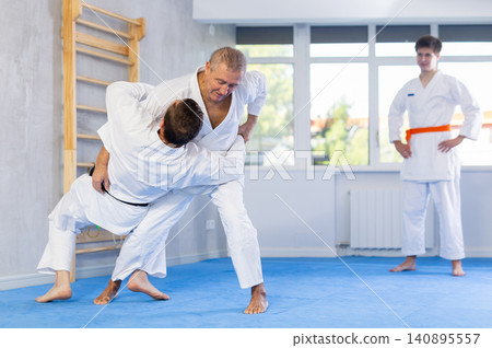 Judo or jiu jitsu classes - two men of different age practicing grabbing and throwing on sports mats Judo or jiu jitsu classes - two men of different age practicing grabbing and throwing on sports mats 140895557