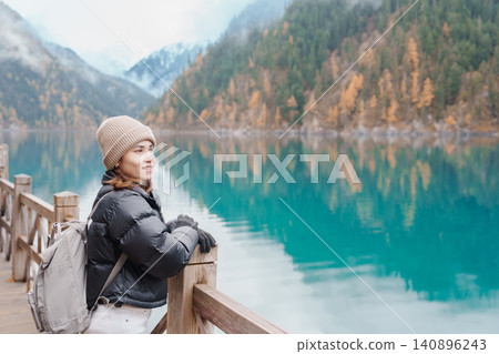 Happy woman traveler travel in jiuzhaigou national park in Sichuan, China. Tourist sightseeing Long lake and snow mountain in Autumn season. Famous Landmark and Vacation near Chengdu, China Happy woman traveler travel in jiuzhaigou national park in Sichuan, China. Tourist sightseeing Long lake and snow mountain in Autumn season. Famous Landmark and Vacation near Chengdu, China 140896243