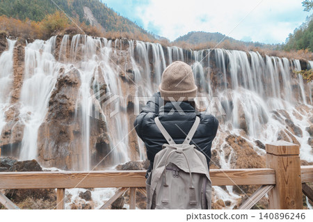 Happy woman traveler travel in jiuzhaigou national park in Sichuan, China. Tourist sightseeing Nuorilang Waterfall in Autumn season. Famous Landmark and Vacation near Chengdu, China Happy woman traveler travel in jiuzhaigou national park in Sichuan, China. Tourist sightseeing Nuorilang Waterfall in Autumn season. Famous Landmark and Vacation near Chengdu, China 140896246