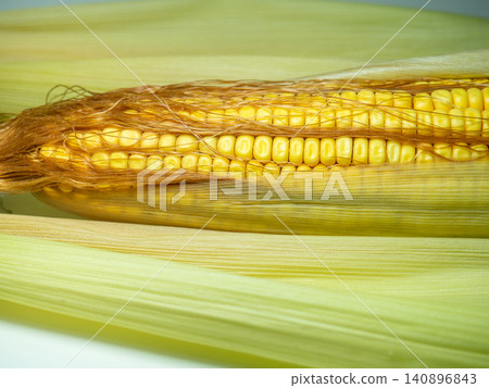 Cereal concept. Semi-husked ripe corn. Corn with leaves. Maize with hairs. Bright yellow grains. Cereal concept. Semi-husked ripe corn. Corn with leaves. Maize with hairs. Bright yellow grains. 140896843