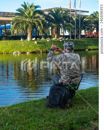 A fisherman removes his fishing rod on the shore of a city pond. Fisherman in Batumi. A fisherman removes his fishing rod on the shore of a city pond. Fisherman in Batumi. 140896955