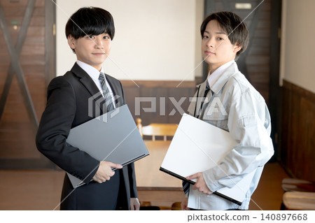A man in a suit holding a laptop and a worker A man in a suit holding a laptop and a worker 140897668