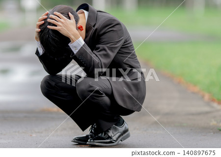 A businessman with his head in his hands outdoors A businessman with his head in his hands outdoors 140897675