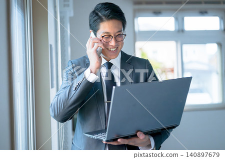 A businessman looking at his computer while on the phone. A businessman looking at his computer while on the phone. 140897679
