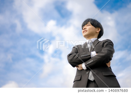 A businessman with his arms crossed under a blue sky A businessman with his arms crossed under a blue sky 140897680