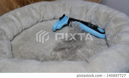 Pet Deshedding Brush and Collected Hair on a Pet Bed 140897727