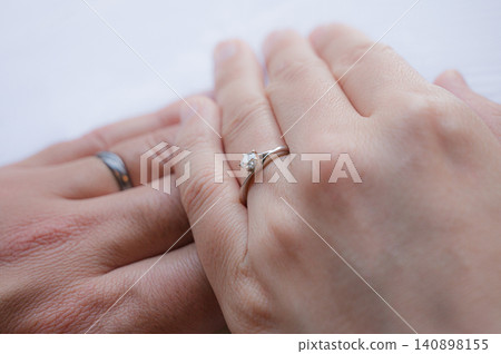 A hand with a wedding ring and an engagement ring stacked together. 140898155