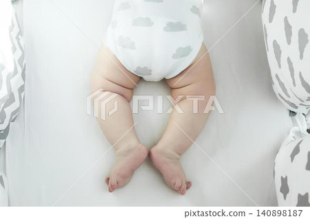 Baby lying on bed with white bedding and patterned pillows Baby lying on bed with white bedding and patterned pillows 140898187
