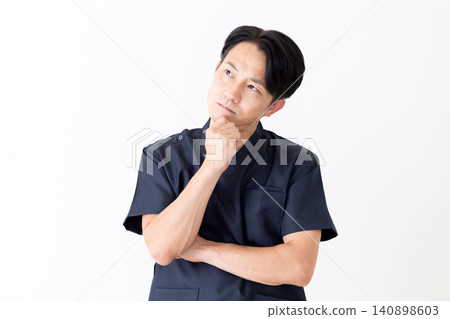 A middle-aged male doctor in navy scrubs, looking troubled. A middle-aged male doctor in navy scrubs, looking troubled. 140898603
