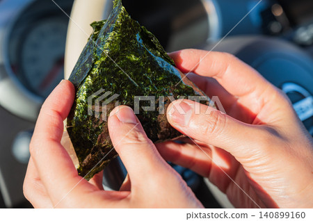 A rice ball wrapped in seaweed, held in the hand inside the car. A rice ball wrapped in seaweed, held in the hand inside the car. 140899160