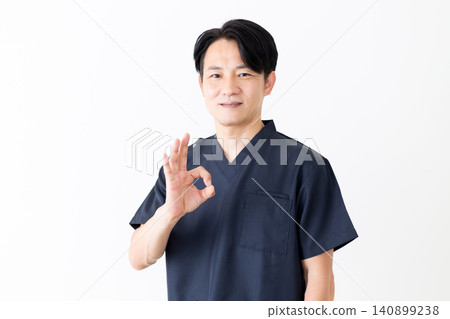 一位身穿海軍藍手術服的中年男醫生擺出了一個圓圈姿勢。 一位身穿海軍藍手術服的中年男醫生擺出了一個圓圈姿勢。 140899238
