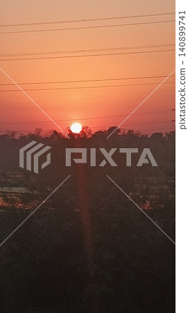 Glowing sun setting behind distant trees and utility lines 140899741