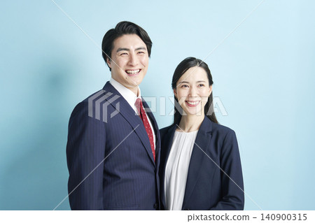 Businesspeople, both male and female, standing side by side with smiles against a light blue background. Businesspeople, both male and female, standing side by side with smiles against a light blue background. 140900315