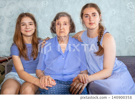 Grandmother with two granddaughters sitting on a couch showing family support and affection Grandmother with two granddaughters sitting on a couch showing family support and affection 140900358