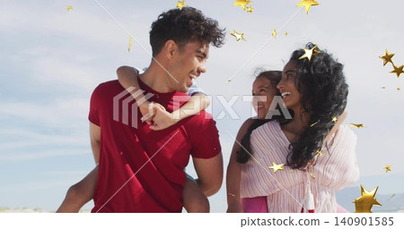 Smiling family standing close together at beach, wearing red T-shirt and pink blouse, gold stars Smiling family standing close together at beach, wearing red T-shirt and pink blouse, gold stars 140901585