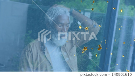 Standing senior man touching head near glass door at home, wearing tan shirt, showing gold stars Standing senior man touching head near glass door at home, wearing tan shirt, showing gold stars 140901610