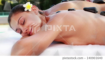 Lying woman client receiving hot stone massage at resort poolside, with basalt stones, plumeria Lying woman client receiving hot stone massage at resort poolside, with basalt stones, plumeria 140901640