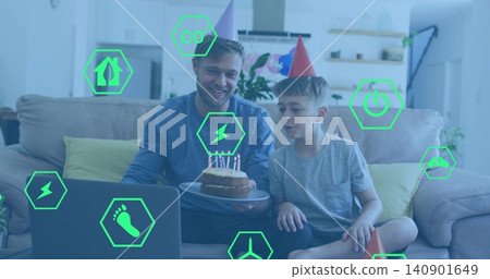 Smiling father-son wearing cone hats, holding cake, leaning blowing candles at home, green AR icons Smiling father-son wearing cone hats, holding cake, leaning blowing candles at home, green AR icons 140901649