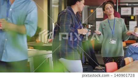 Talking two women in plaid and green clothing holding takeaway cups with lanyard in office breakout 140901728