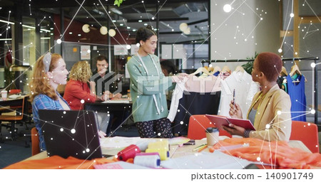 Presenting woman in green showing two-tone skirt on hanger at studio table, with garment rack Presenting woman in green showing two-tone skirt on hanger at studio table, with garment rack 140901749