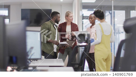 Reviewing documents, four coworkers in bright clothes checking laptop tablet papers in open office Reviewing documents, four coworkers in bright clothes checking laptop tablet papers in open office 140901769