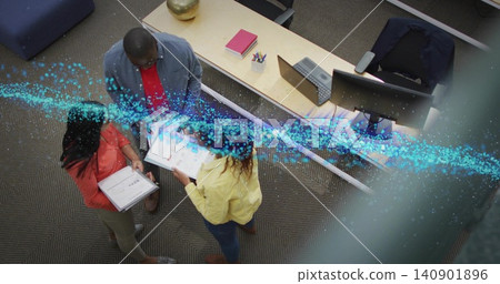 Reviewing three coworkers in office clothes at open-plan desk holding papers, laptop, blue overlay 140901896