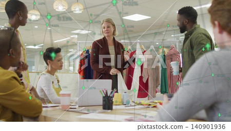 Holding white garment, lead presenter in brown cardigan leading review at office with clothing rack Holding white garment, lead presenter in brown cardigan leading review at office with clothing rack 140901936
