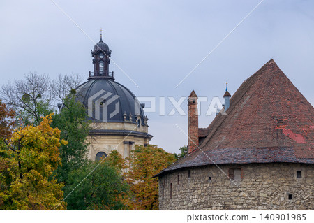 A view of an old European city featuring a grand dome and a rustic stone tower, surrounded by trees in fall colors A view of an old European city featuring a grand dome and a rustic stone tower, surrounded by trees in fall colors 140901985