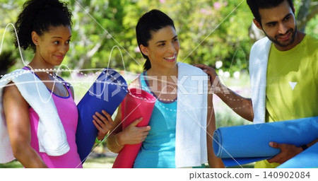 Standing three adults in athletic wear holding rolled yoga mats and towels in sunlit park, smiling Standing three adults in athletic wear holding rolled yoga mats and towels in sunlit park, smiling 140902084