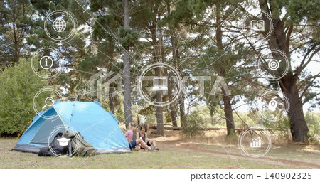 Sitting two women wearing shorts, shirts in pine clearing, with blue tent, backpacks and HUD icons Sitting two women wearing shorts, shirts in pine clearing, with blue tent, backpacks and HUD icons 140902325