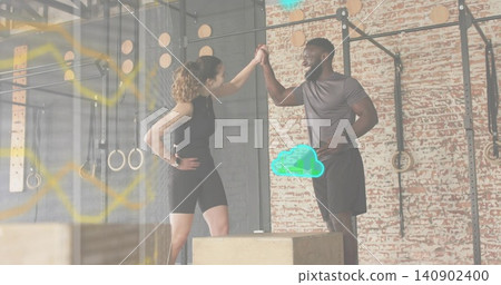 High-fiving workout partners wearing athletic clothing in warehouse gym, with plyo boxes and rig High-fiving workout partners wearing athletic clothing in warehouse gym, with plyo boxes and rig 140902400