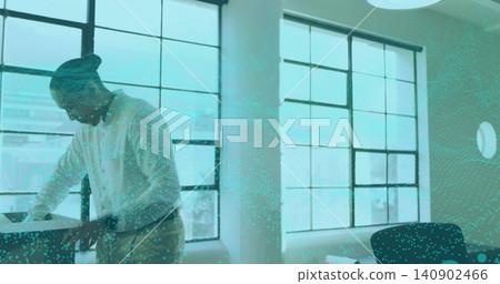 Leaning worker wearing light shirt, pants reviewing papers at desk by windows, with teal overlay Leaning worker wearing light shirt, pants reviewing papers at desk by windows, with teal overlay 140902466