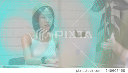 Typing Asian woman wearing knit beanie and round eyeglasses, using laptop at small meeting area 140902468