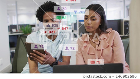 Reviewing coworkers analyzing social icons on tablet and laptop at office, in polo and pink blouse Reviewing coworkers analyzing social icons on tablet and laptop at office, in polo and pink blouse 140902696