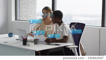 Reviewing women in dotted beige blouses checking documents at office desk with laptop notifications Reviewing women in dotted beige blouses checking documents at office desk with laptop notifications 140902697