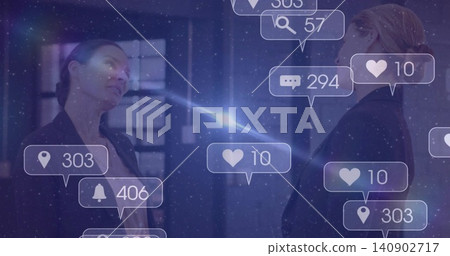 Standing two women in blazers facing each other in office, showing notification bubbles, lens flare Standing two women in blazers facing each other in office, showing notification bubbles, lens flare 140902717