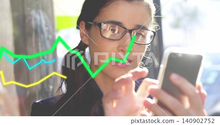 Holding phone, woman wearing dark jacket, glasses tapping screen by wall on street, colored charts Holding phone, woman wearing dark jacket, glasses tapping screen by wall on street, colored charts 140902752