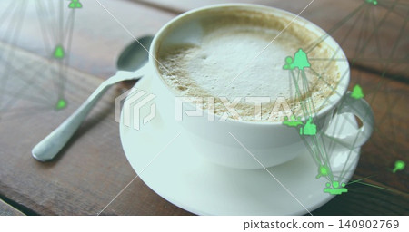 Showing ceramic cup sitting on dark table, holding frothy latte, saucer, metal spoon, green overlay 140902769