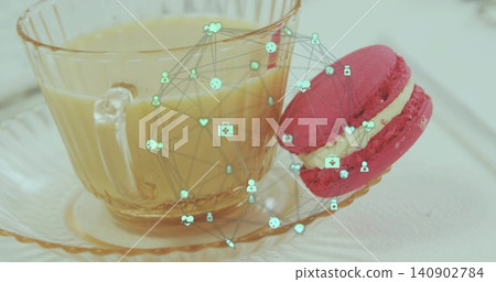 Displaying glass teacup holding pale beverage on tabletop, featuring pink macaron and teal overlay Displaying glass teacup holding pale beverage on tabletop, featuring pink macaron and teal overlay 140902784