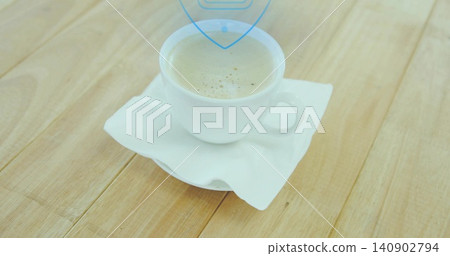 Sitting white ceramic cup holding light-brown coffee with thin crema on napkin at kitchen table Sitting white ceramic cup holding light-brown coffee with thin crema on napkin at kitchen table 140902794