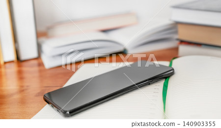 Black smartphone screen down on a table with books in background 140903355