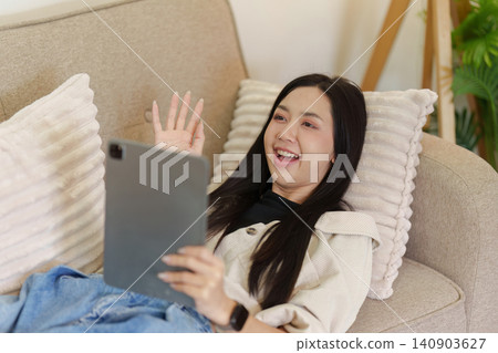 Asian woman waving hand during video call on tablet at home Asian woman waving hand during video call on tablet at home 140903627